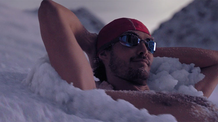 a shirtless man in a swim cap and goggles relaxing in the snow