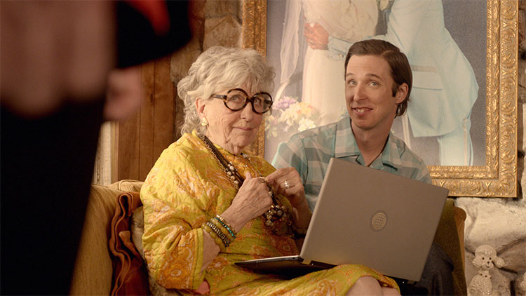 a middle aged white man and an old lady with a laptop sitting in her living room
