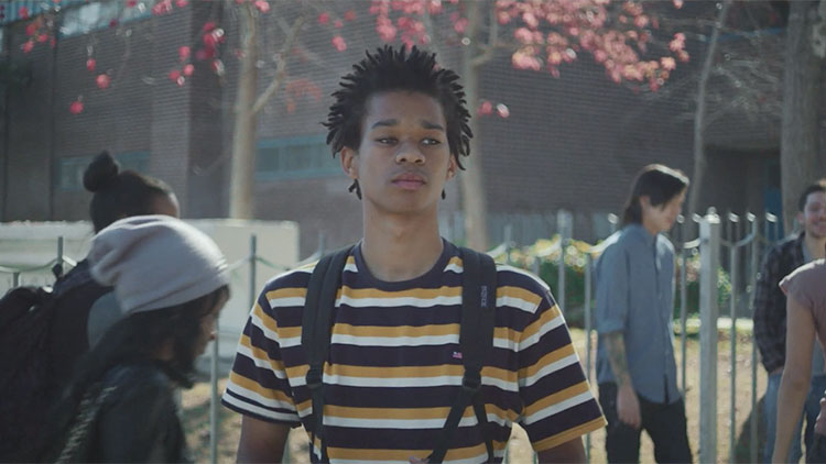 a black teenager with a horizontally striped shirt and a backpack