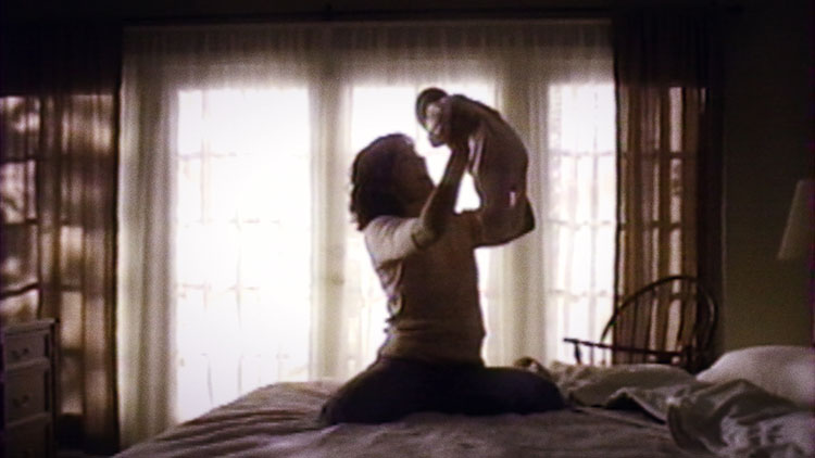 a mother in a bedroom holding her baby above her