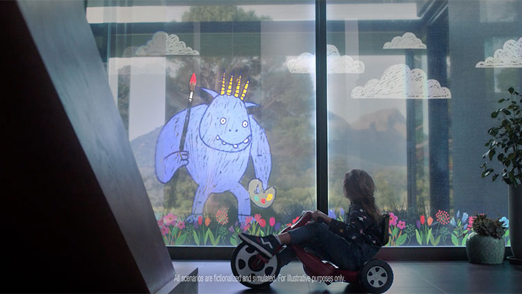 a young girl on a big wheel tricycle looking at a painting of a friendly blue monster on a window