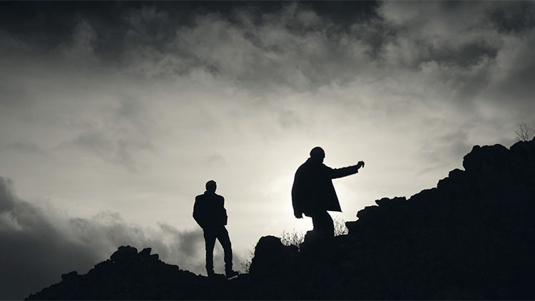 the silhouettes of two older men walking along a rocky hill